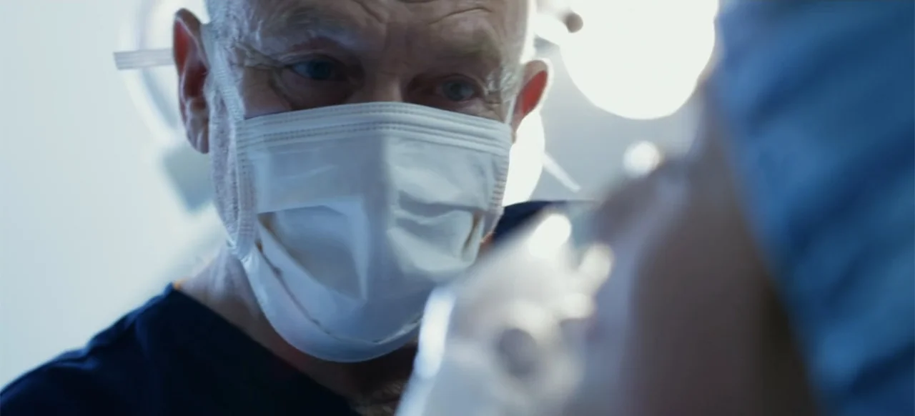 The Russian Bride (2019) movie still: closeup — An operating room featuring bright overhead surgical lights and medical professionals in blue…