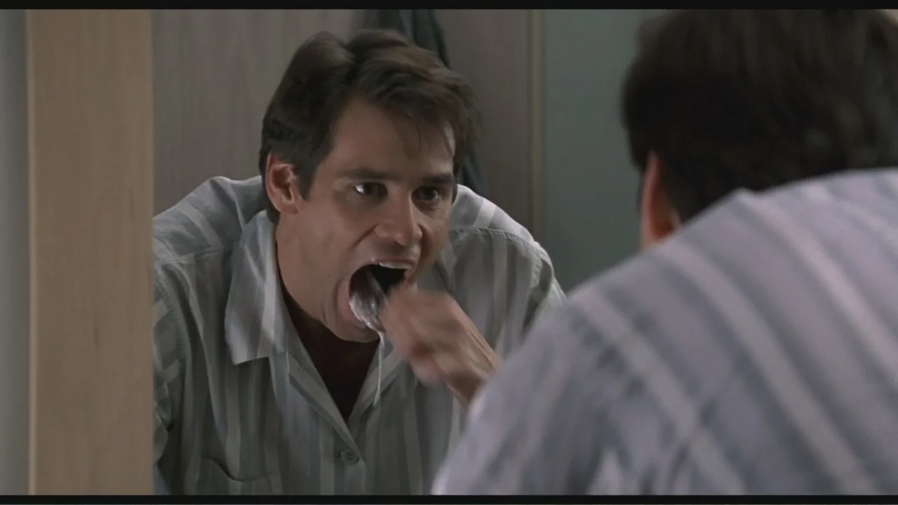 Liar Liar (1997) movie still: medium — A residential bathroom features a large wall-mounted mirror above a sink basin. A man stands before the…