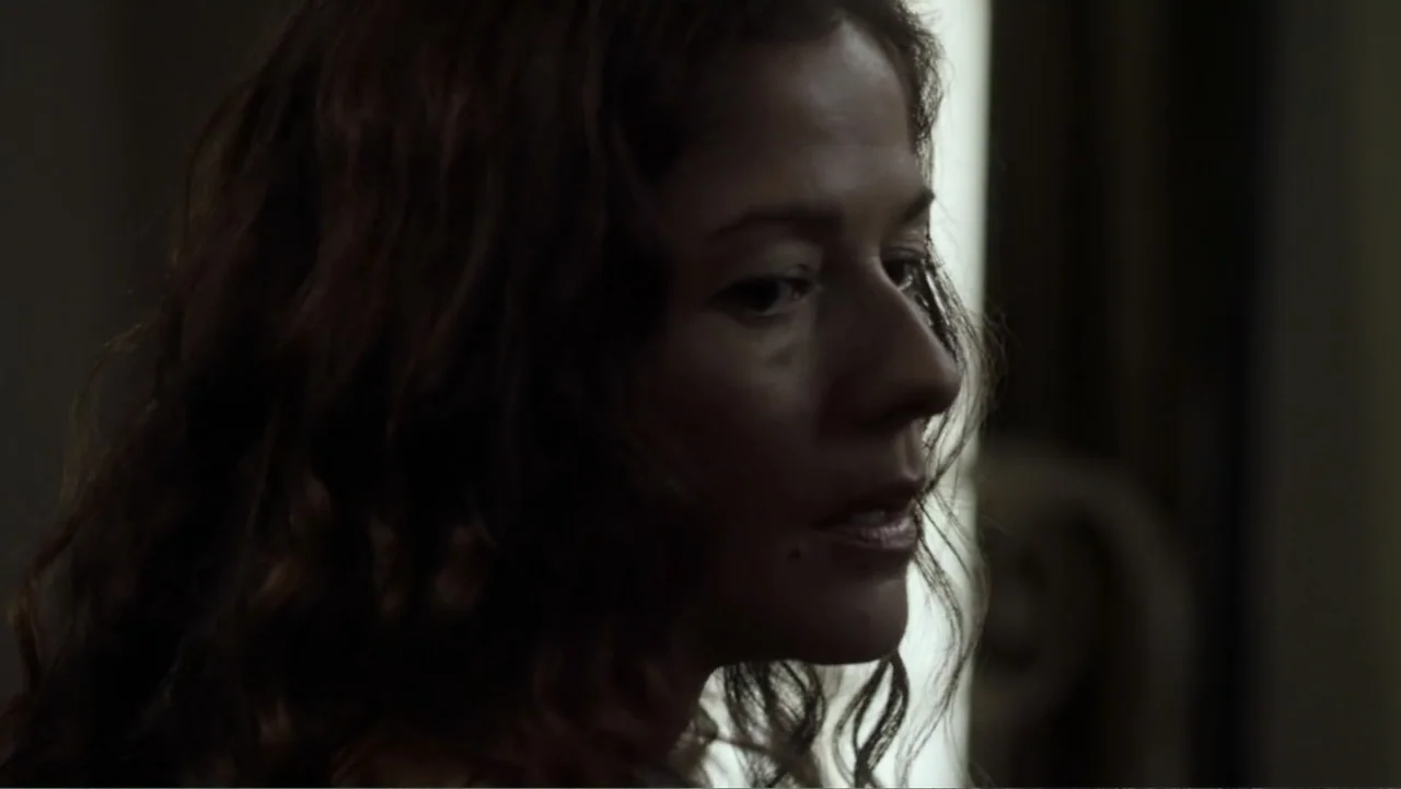 Dawn Rider (2012) movie still: closeup — A dimly lit interior space with a soft light source from a window. A woman looks off-camera while her face…