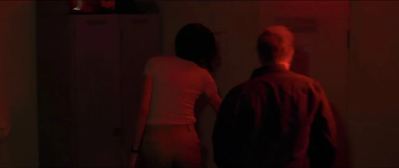 Primal (1994) movie still: medium — A dimly lit room with lockers and papers attached to the wall. Two people stand close to the wall examining…