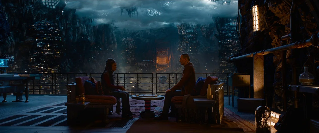 The Matrix Resurrections (2021) movie still: wide — A high-rise balcony overlooks a vast, glowing subterranean industrial city with dense structural…