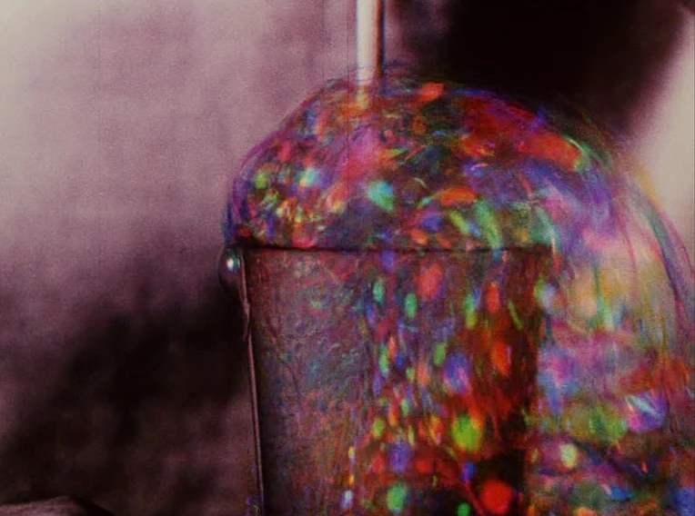 Daisies (1966) movie still: closeup — A metal container overflows with iridescent, multi-colored soap bubbles in a dark space. A thin glass rod…