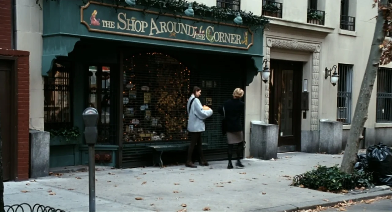 You've Got Mail (1998) movie still: wide — A green wooden storefront with a large sign reading The Shop Around the Corner. Two women stand on the…