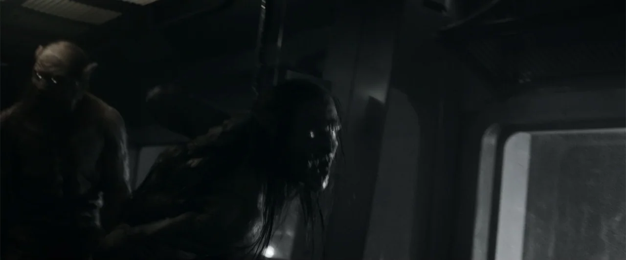Howl (2015) movie still: medium — A dark industrial corridor features metallic surfaces and geometric structures in a dimly lit space. Two creatures…