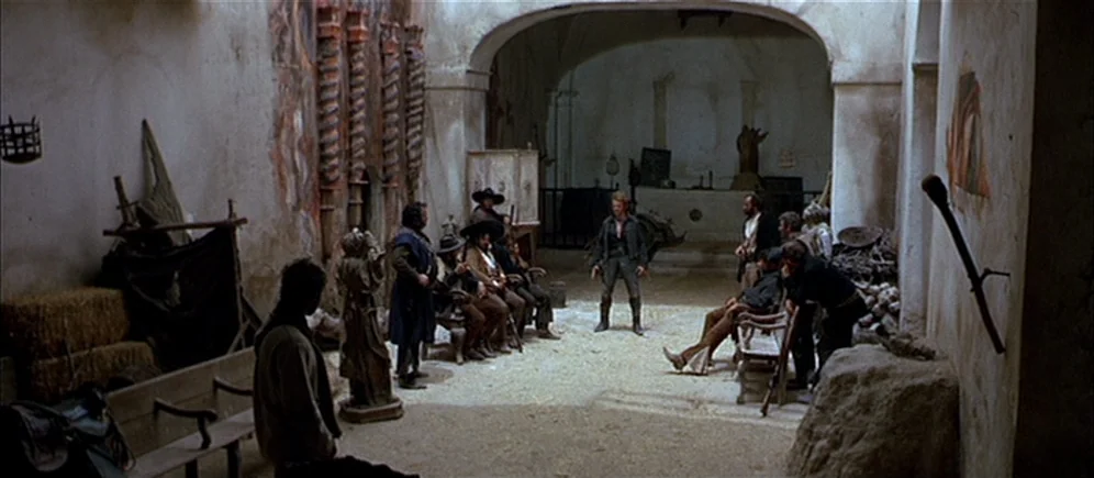 For A Few Dollars More (1965) movie still: wide — A stone-walled interior with arched ceilings and rustic wooden furniture scattered around. A man…