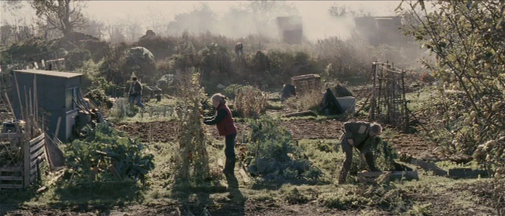 Another Year (2010) movie still: wide — A rural community allotment features raised vegetable beds, wooden trellises, and a small shed. Multiple…