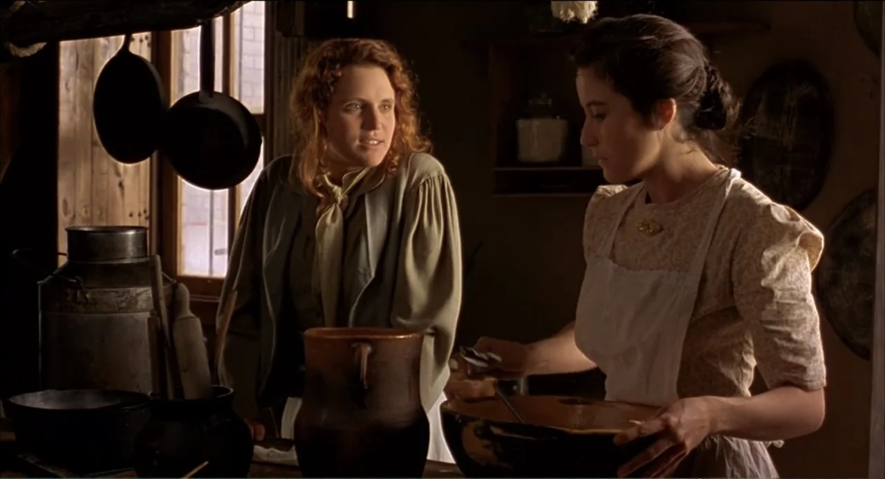 Like Water for Chocolate (1992) movie still: medium — A rustic interior with wooden surfaces and iron cookware hanging near a window. Two women in…
