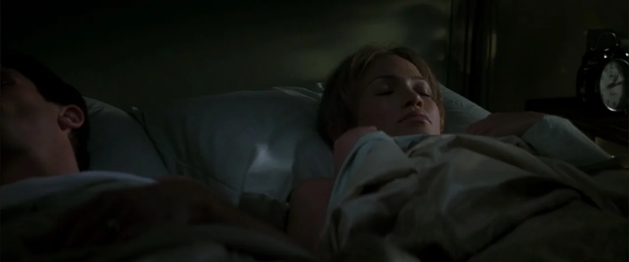 Enough (2002) movie still: medium — A dimly lit bedroom features two people sleeping side by side in a bed. The figures rest under covers with an…