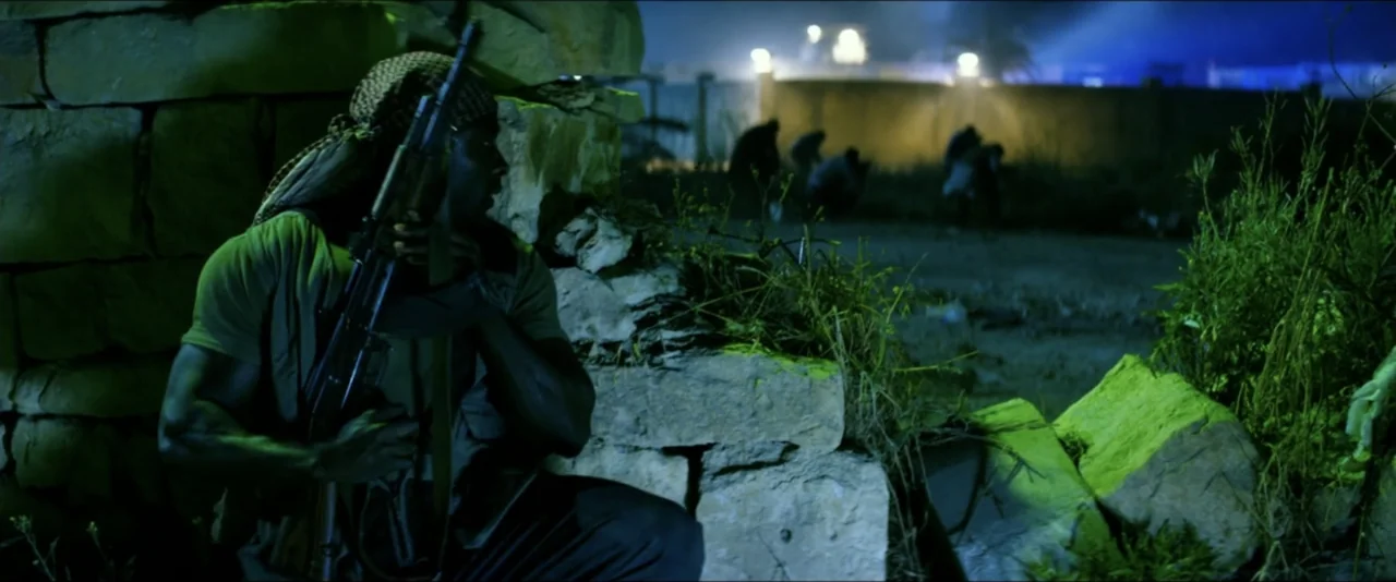 13 Hours: The Secret Soldiers of Benghazi (2016) movie still: medium — A man hides behind a stack of stones at night under artificial green light.…