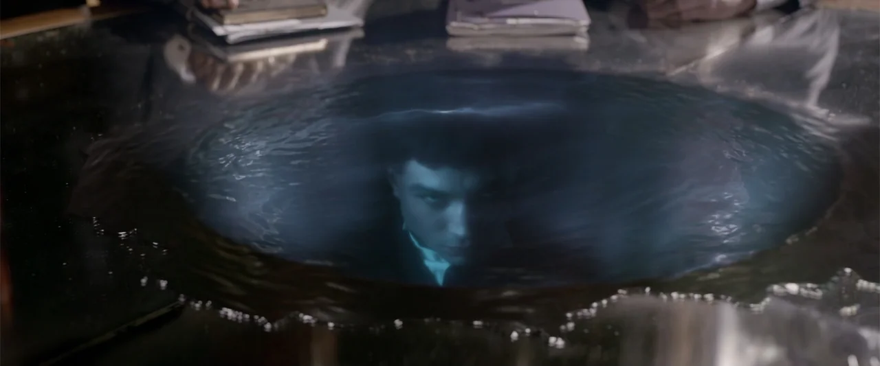 Fantastic Beasts: The Crimes of Grindelwald (2018) movie still: closeup — A dark, reflective table holds a swirling pool of liquid that acts as a…