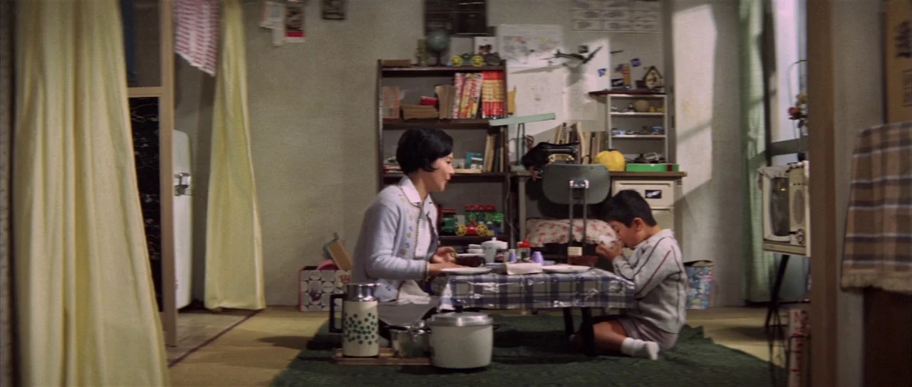 All Monsters Attack (1969) movie still: wide — A modest Japanese apartment with tatami mats features a low dining table and shelves. An adult woman…