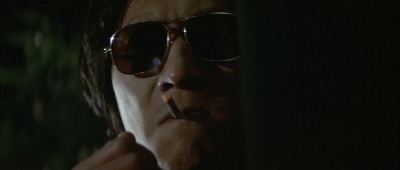 Godzilla Vs Mechagodzilla (1974) movie still: closeup — A dark outdoor space at night with a man partially obscured by shadow. He wears sunglasses…