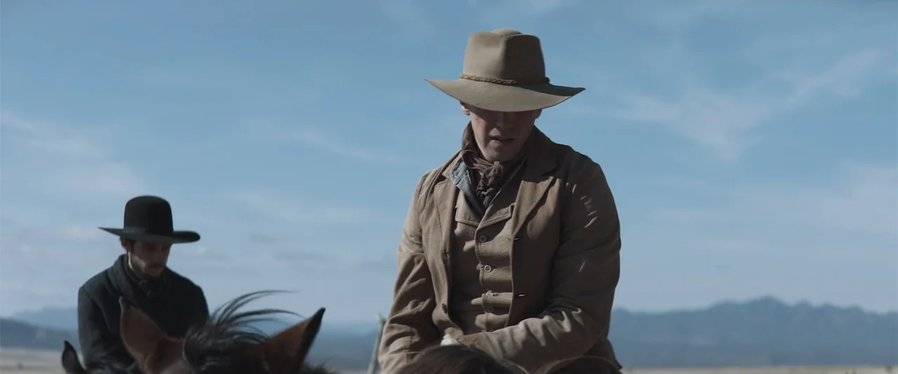 The Wind (2005) movie still: medium — An open desert landscape serves as the backdrop for two men riding horses. The men wear mid-19th-century…