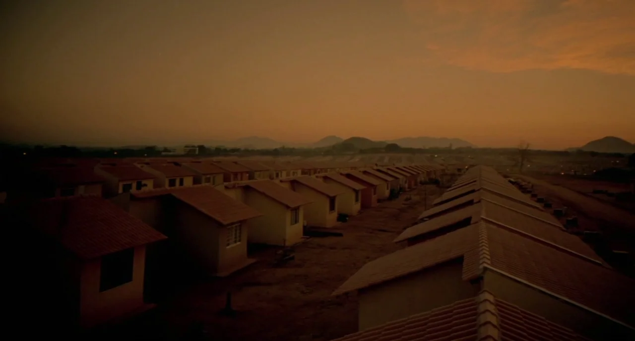 City of God (2002) movie still: establishing — A dense suburban neighborhood features rows of identical small houses with tiled roofs. The scene…