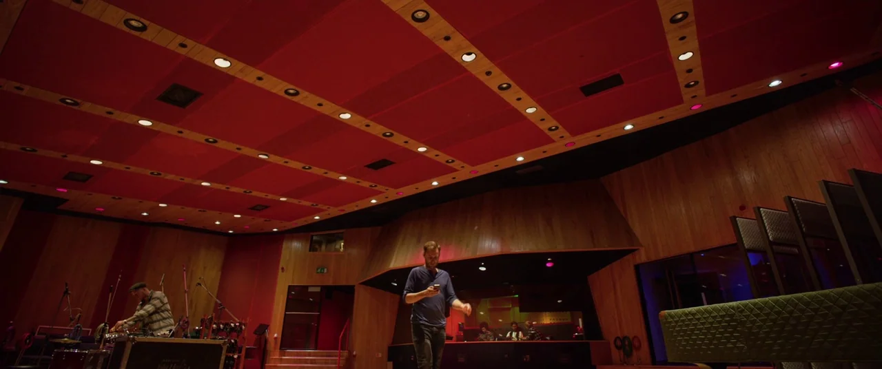 Yesterday (2019) movie still: wide — A spacious recording room with high wooden walls and red acoustic paneling on ceiling. A man walks through the…