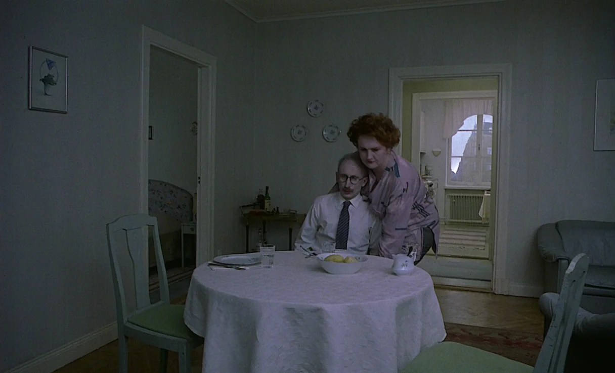 Songs from the Second Floor (2000) movie still: medium — An interior dining area with light-colored walls and a round table with a tablecloth. A…