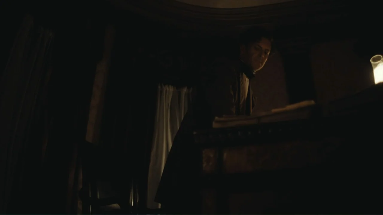 Demon in the White House (2021) movie still: medium — A dark study features a wooden desk and a single lit candle in frame. A man in…