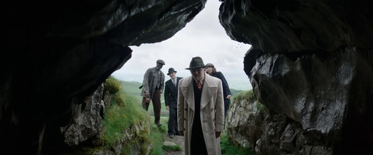 Nandor Fodor and the Talking Mongoose (2023) movie still: medium — A group of people dressed in 1940s attire emerge from a jagged rock opening. The…