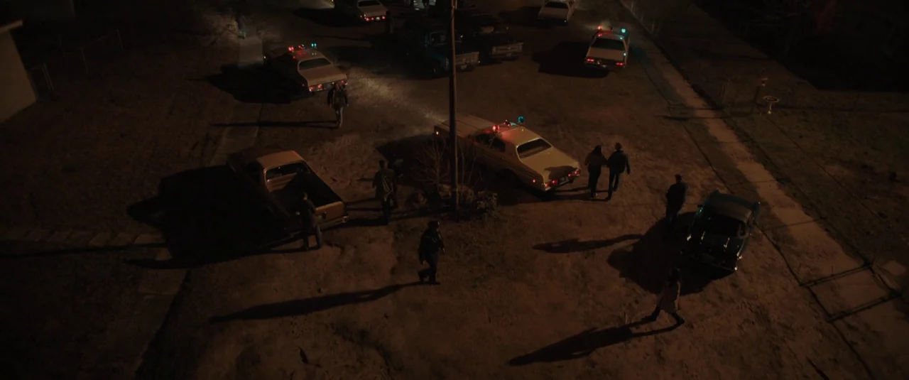 The Black Phone (2021) movie still: wide — A suburban residential street at night is filled with several parked vehicles and people. Police cruisers…