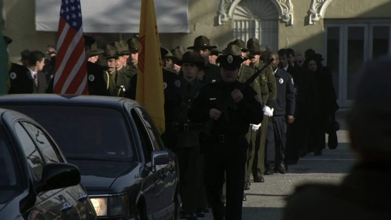The Shepherd (2023) movie still: medium — A group of police officers marches in a formal procession along a paved road. Officers in dark uniforms…