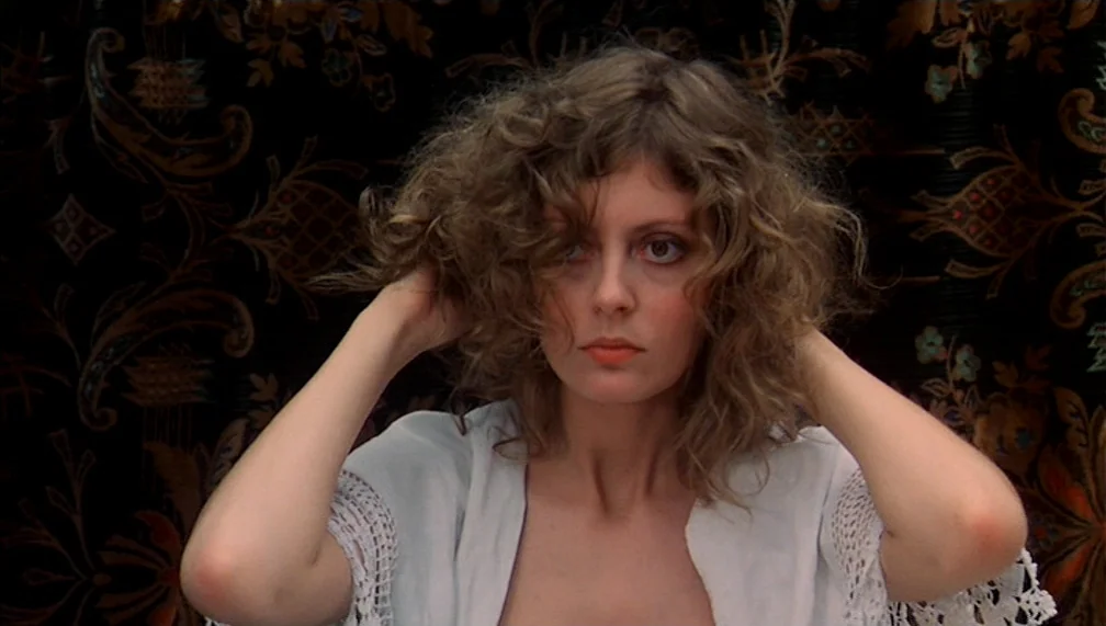 Pretty Baby (1978) movie still: closeup — A woman stands before a dark patterned curtain with intricate gold and floral designs. She holds both…
