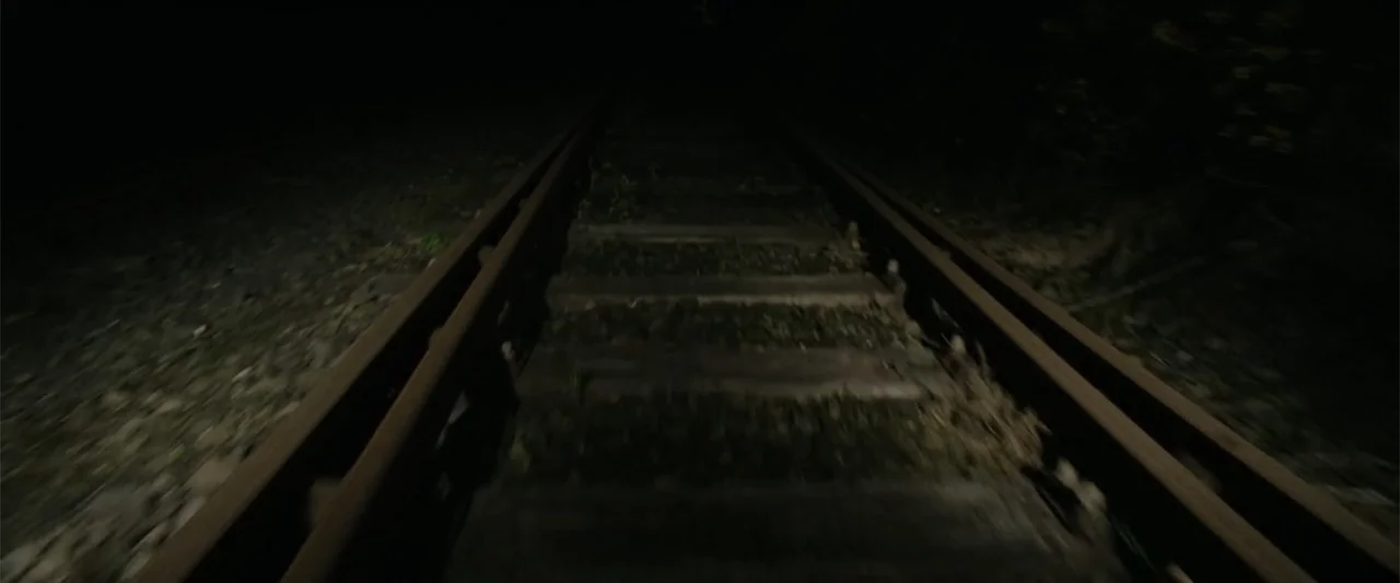 Freud's Last Session (2023) movie still: establishing — Dark and weathered railroad tracks extend into the distance through an unlit landscape. The…