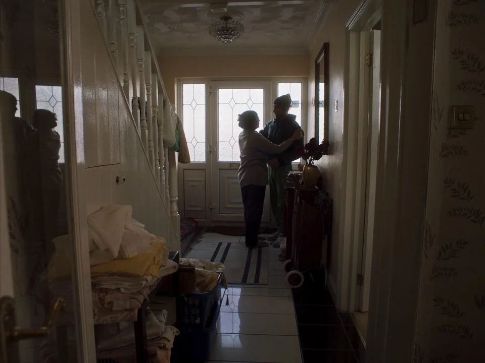 Mogul Mowgli (2020) movie still: fullbody — A residential tiled foyer with a staircase to the left and a glass door. A woman stands face-to-face…