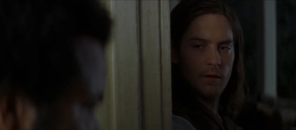 Ride With The Devil movie still: medium — A dimly lit interior space features a wooden door frame partially obscuring a man. The man looks toward…
