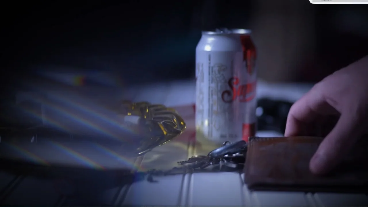 Murder at Carter County Mines (2023) movie still: closeup — A white slatted table holds a beer can, a glass ashtray, keys, and a wallet. A hand…