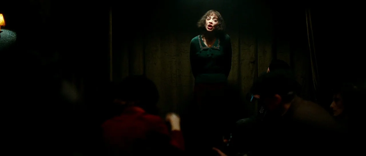 La Vie En Rose (2007) movie still: medium — A dimly lit club with dark curtains serving as a backdrop for a performer. A woman stands in a pool of…