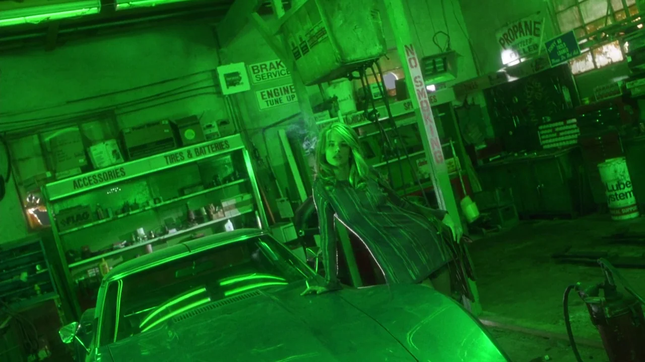 Natural Born Killers (1994) movie still: medium — A cluttered automotive workshop is illuminated entirely by intense, glowing green artificial…