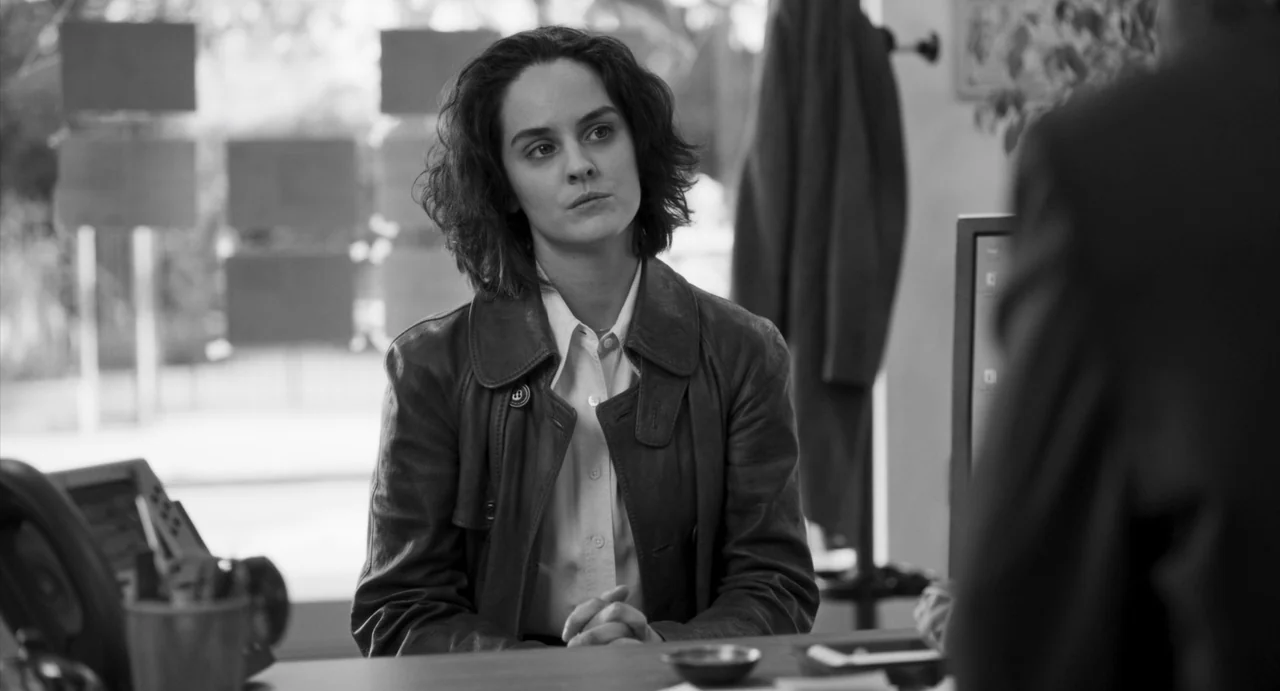 Paris, 13th District (2021) movie still: medium — A modern workspace with a desk and a coat rack visible in the background. A woman in a leather…