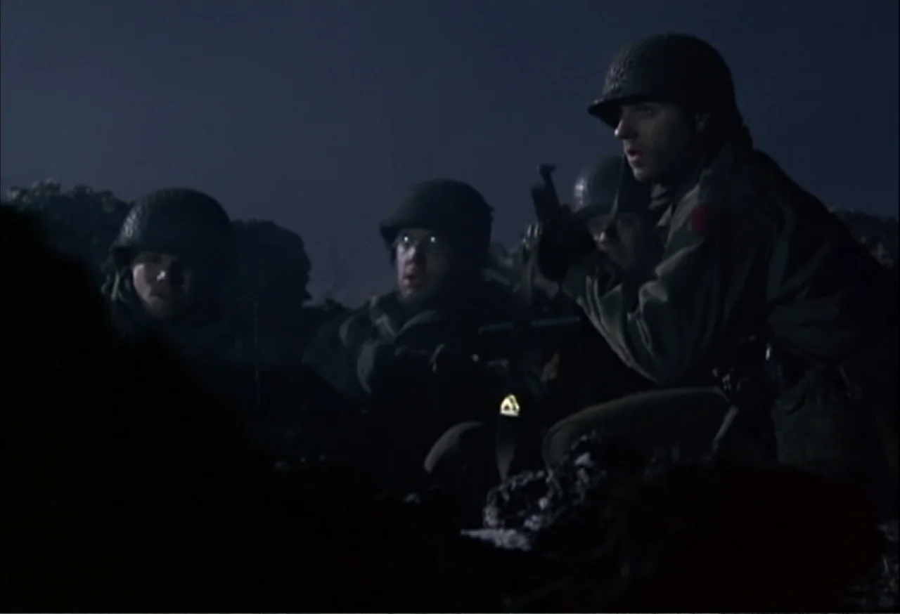When Trumpets Fade (1998) movie still: medium — Three soldiers crouch in a dark, uneven field under a dim night sky. The men hold their weapons…