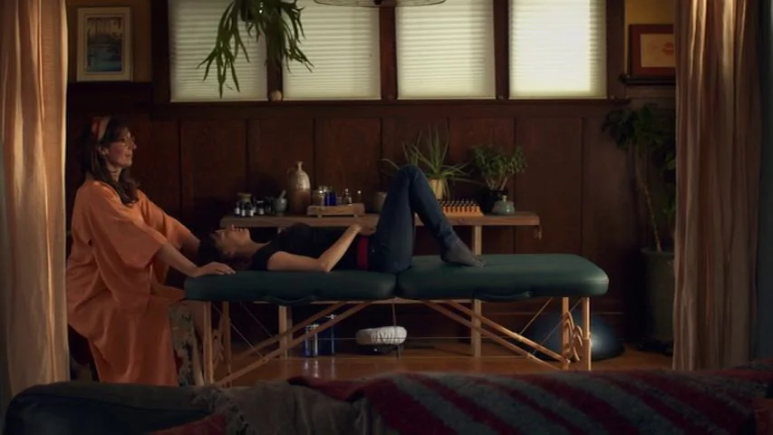 Touchy Feely (2013) movie still: medium — A therapy space features dark wood paneling, a massage table, and various potted plants. A woman performs…