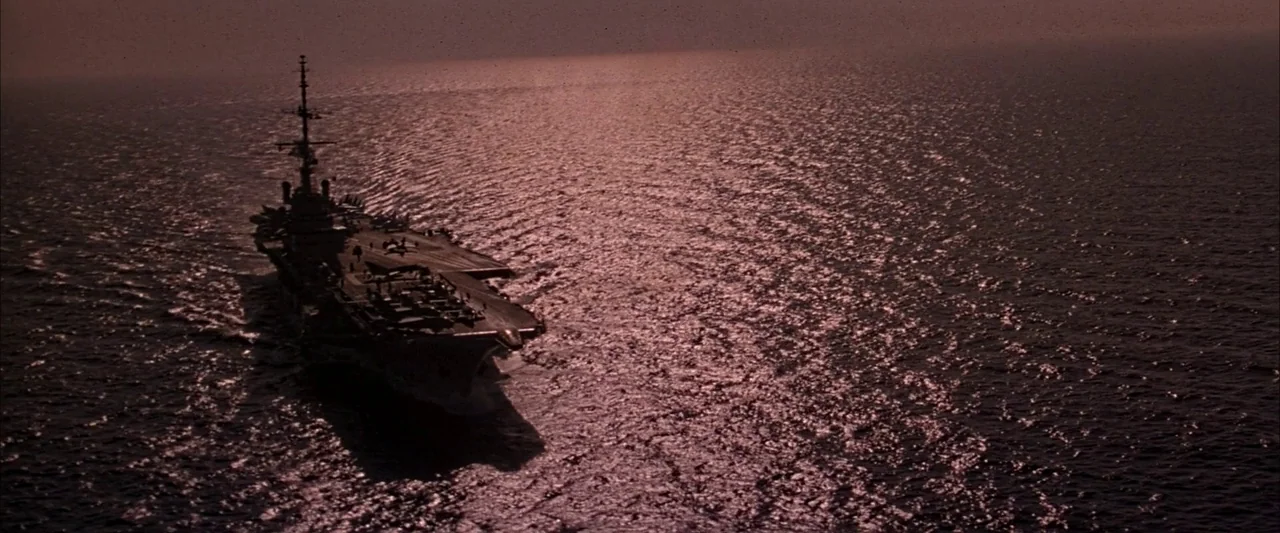 Crimson Tide (1995) movie still: wide — A military aircraft carrier travels through the open ocean during the late afternoon. The vessel is captured…
