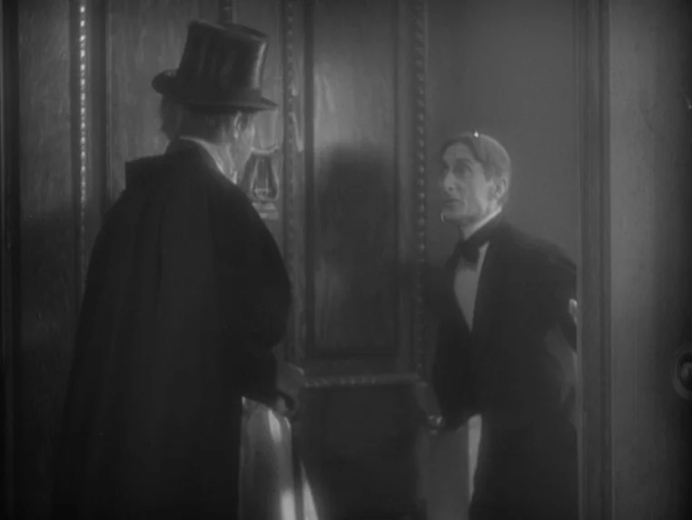 Dr. Jekyll and Mr. Hyde (1931) movie still: medium — A dark interior doorway with ornate wood paneling and a small harp carving. A man in a tuxedo…