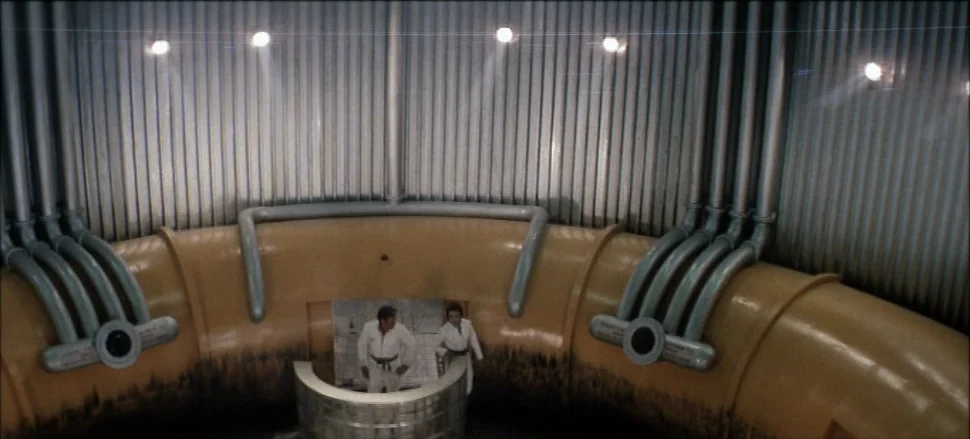 Solaris (1972) movie still: wide — A curved industrial corridor features bright yellow piping and corrugated metal walls. Two men in white jumpsuits…