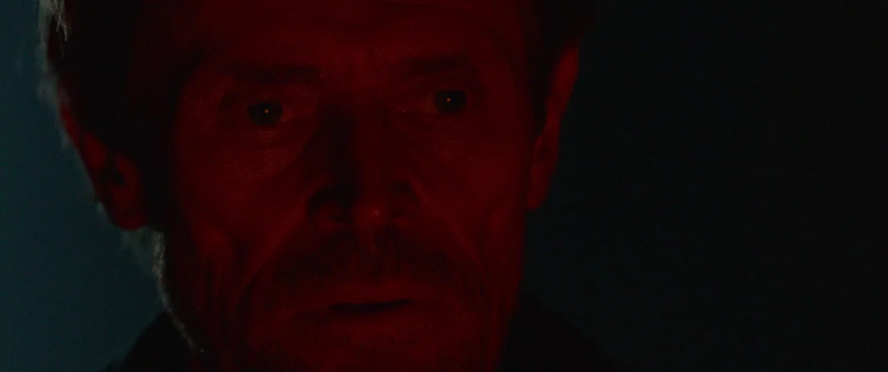 Siberia (2019) movie still: closeup — A man's face is shown in close proximity against a pitch black background. Red lighting highlights his…