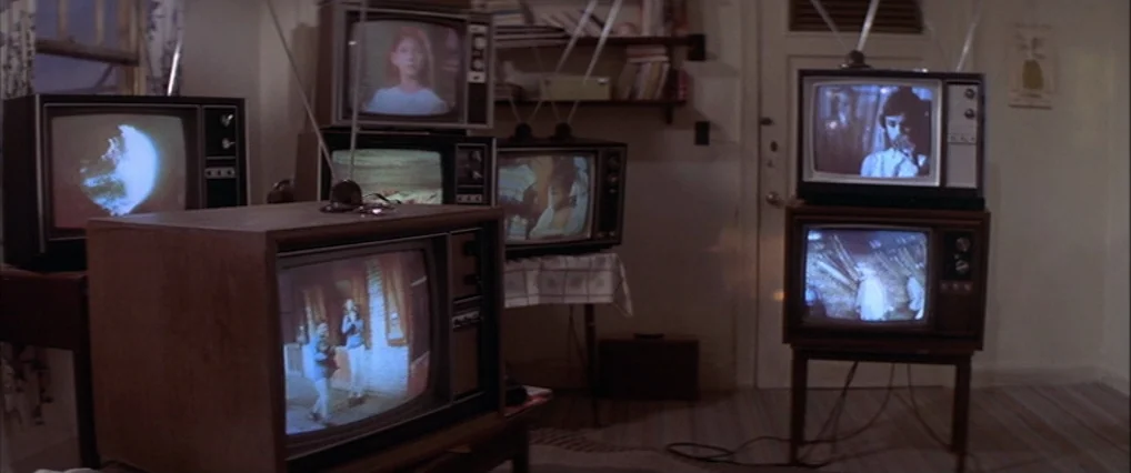 The Man Who Fell To Earth (1976) movie still: wide — A domestic space is filled with several vintage wooden televisions displaying various video…