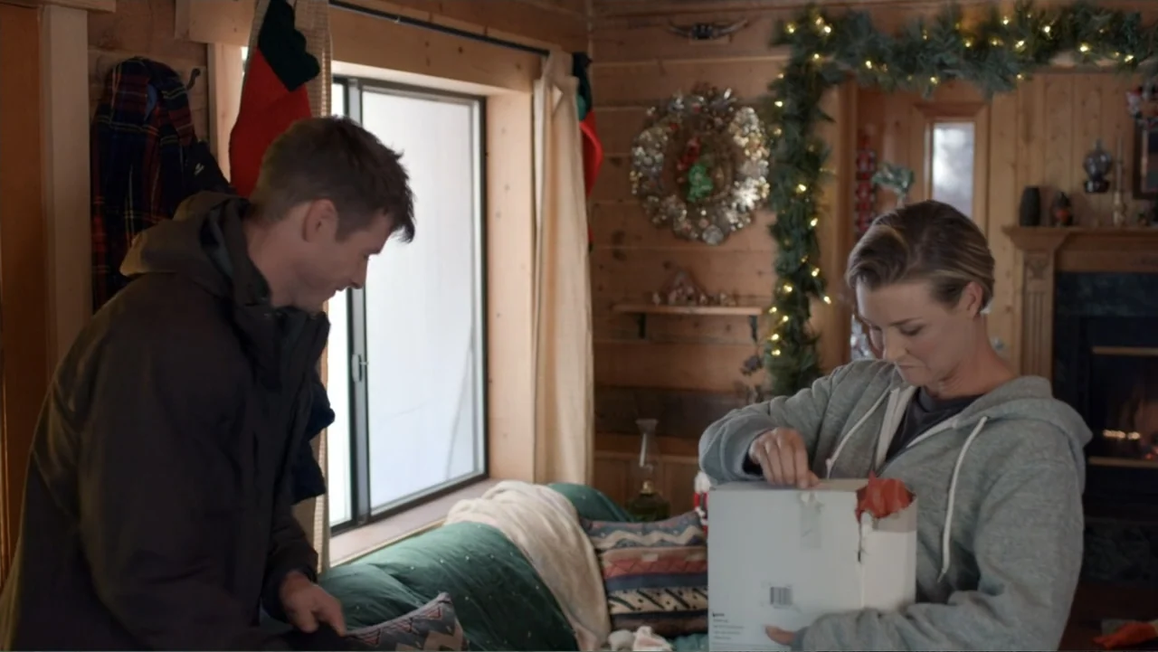 Alex & Emma (2003) movie still: medium — A wood-paneled room decorated for the holidays with a fireplace and festive garlands. A man in a brown…