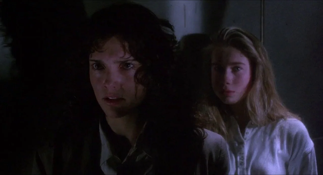 Hellbound: Hellraiser II (1988) movie still: medium — A dark hallway with minimal light sources and indistinct walls behind two women. The two women…