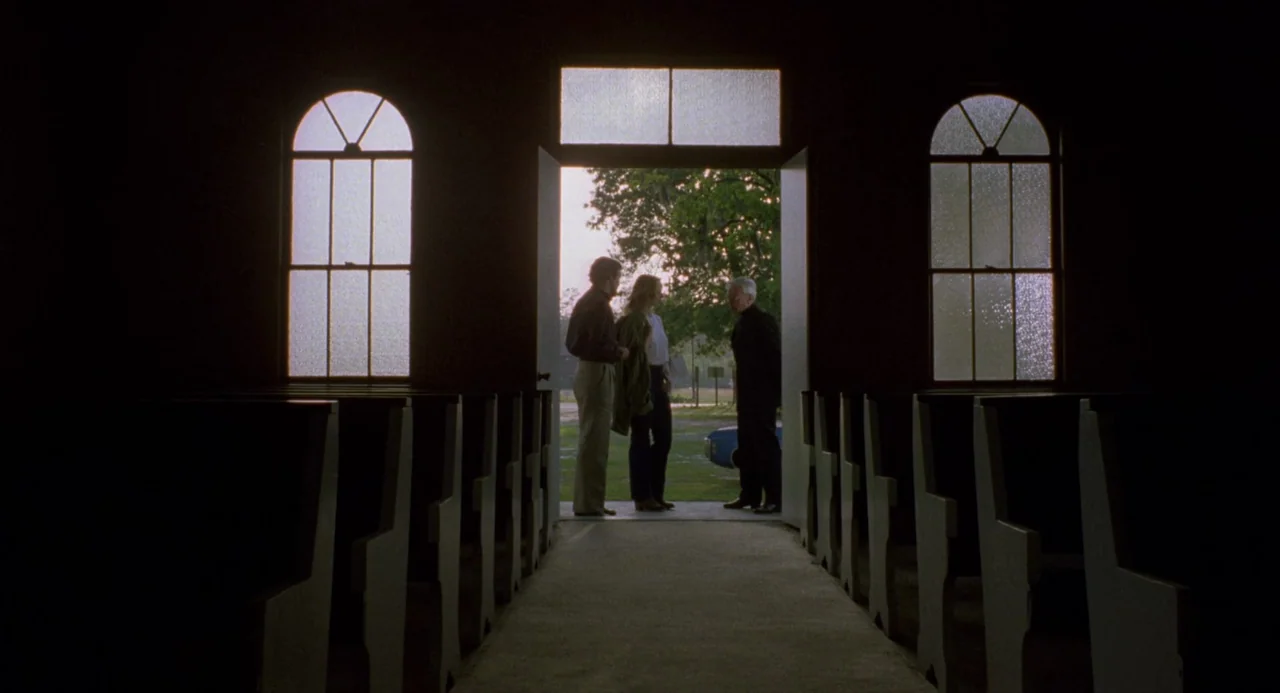 City of the Living Dead (1980) movie still: wide — A dimly lit church interior with wooden pews facing a brightly lit open doorway. Three people…
