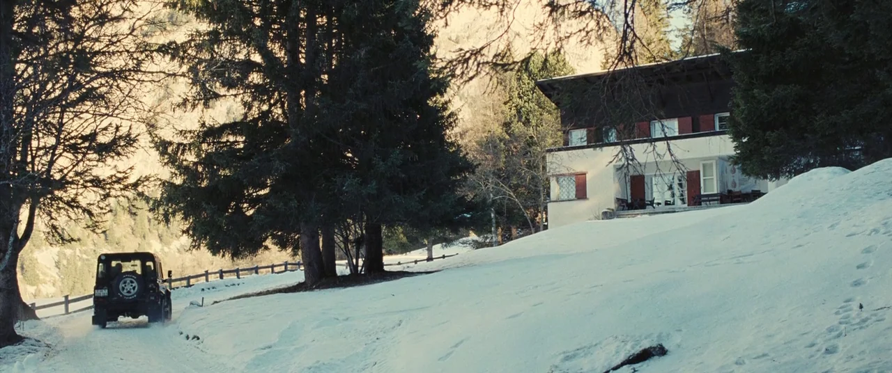 Clouds of Sils Maria (2014) movie still: wide — A white chalet with dark wooden accents sits on a snowy mountain slope. A dark off-road vehicle…