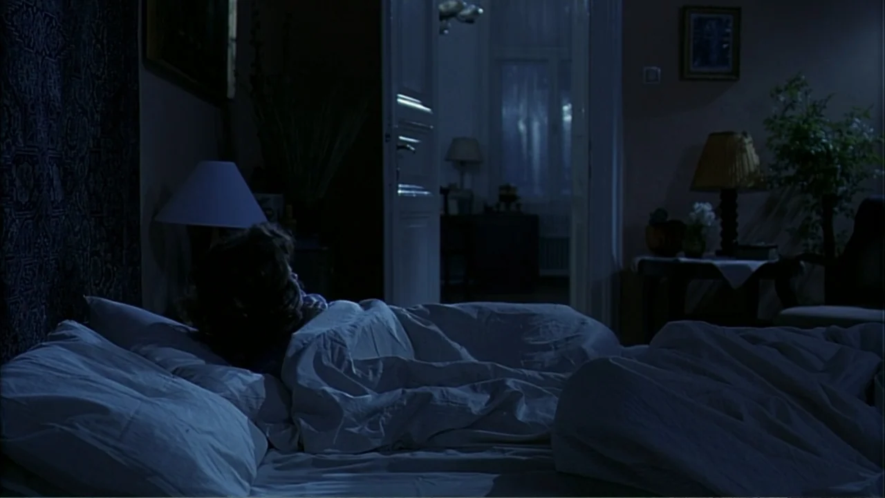 Citizen X (1995) movie still: medium — A dark bedroom at night with a person asleep under white bedsheets. The person faces away from the camera…