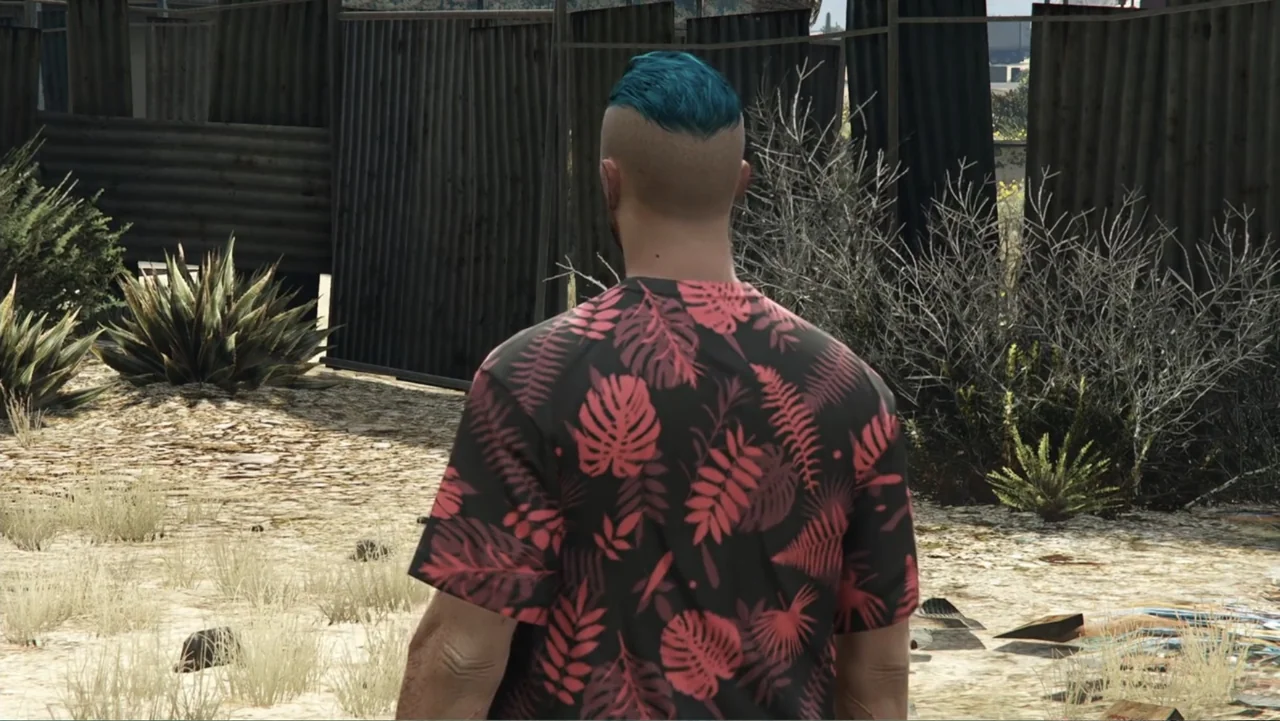 Grand Theft Hamlet (2024) movie still: medium — A dry, dusty exterior with corrugated metal barriers and scattered desert vegetation. A man with a…