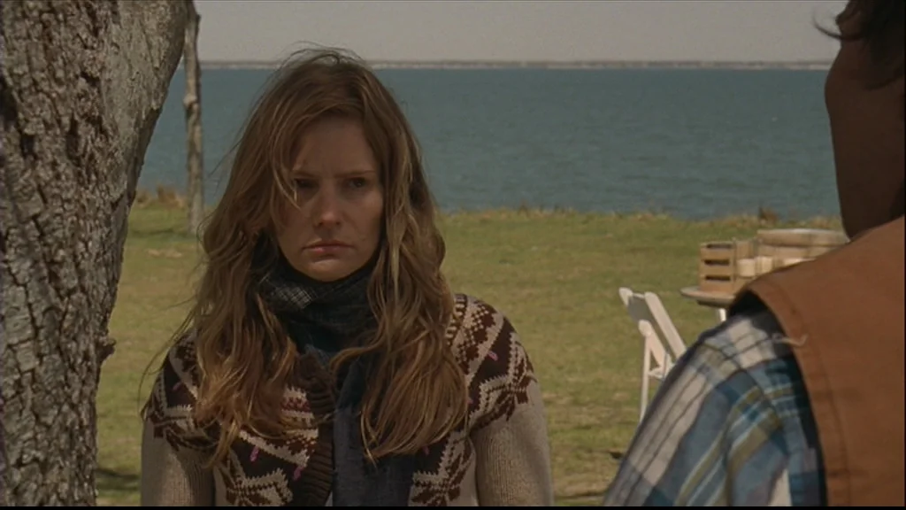 Margot At The Wedding (2007) movie still: medium — A woman stands by a large tree with a lake in the background. She listens as a man partially out…