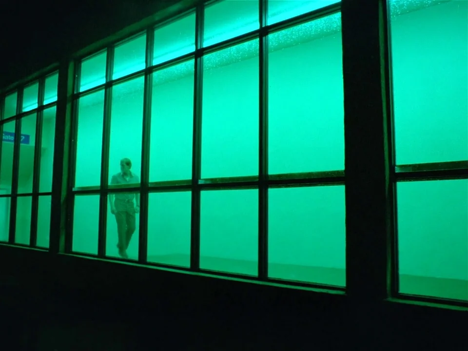 One From The Heart (1982) movie still: wide — A long glass-walled structure at night is bathed in an intense green artificial light. A man walks…