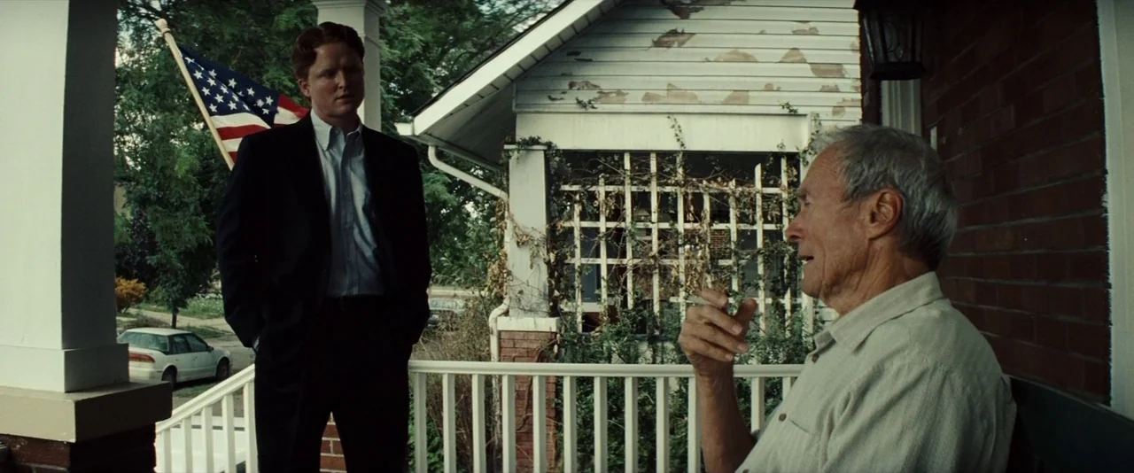 Gran Torino (2008) movie still: medium — A residential porch features white railings and a wooden latticework partition behind the men. One man in a…