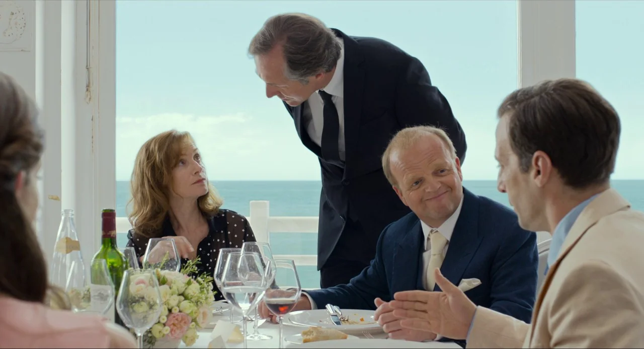 Happy End (2017) movie still: medium — A seaside restaurant features a large panoramic window showing the blue ocean horizon. A man stands while…