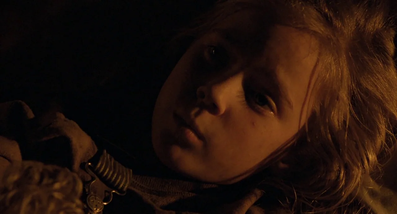 Aliens (1986) movie still: closeup — A child rests in near darkness with minimal light catching their facial features. The subject lies supine and…